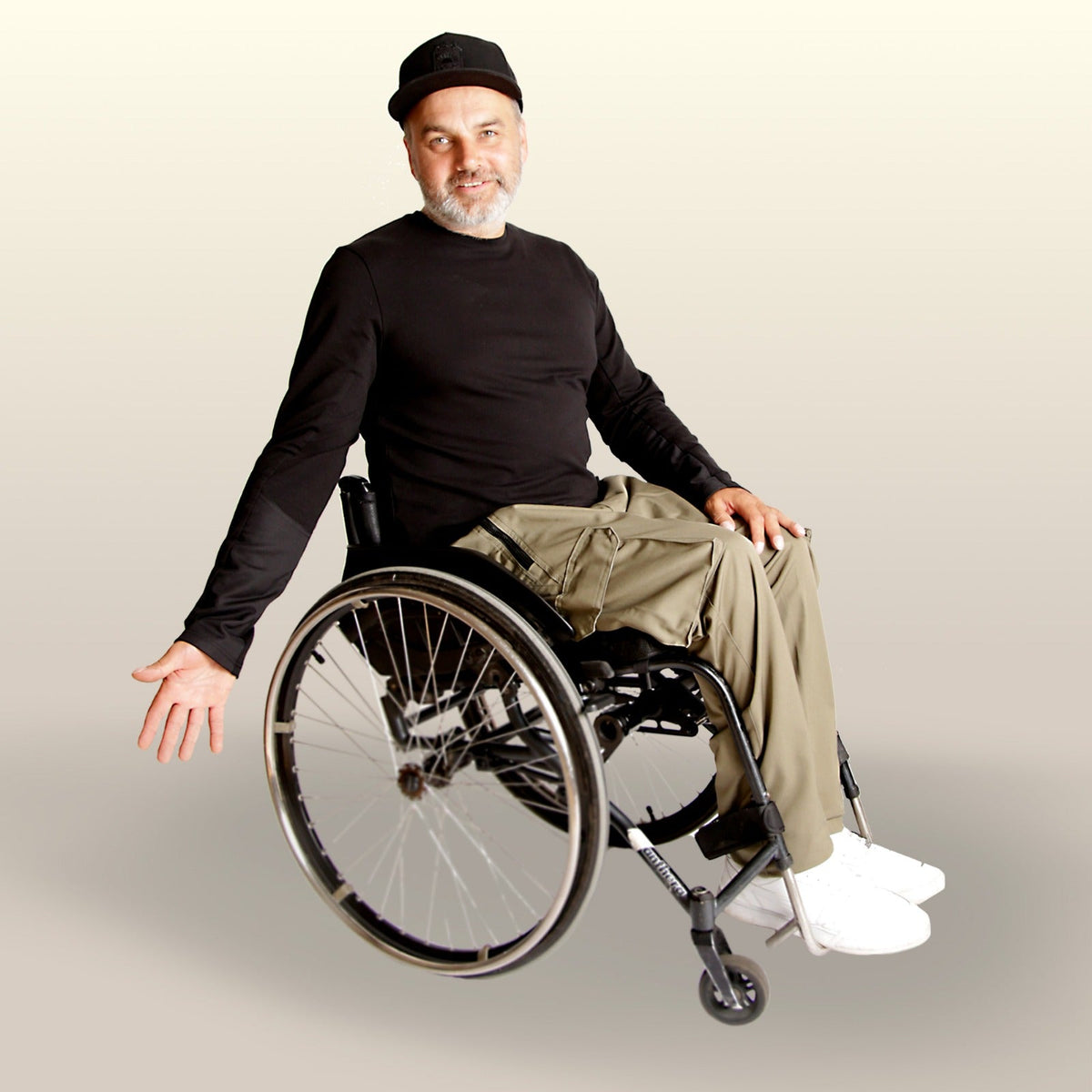 A smiling man in a wheelchair showcasing adaptive clothing made by Vilber's featuring adaptive pants in olive color and black shirt with cordura sleeves